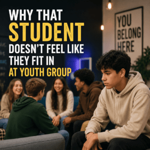 Teen sitting apart from a diverse group of students in a youth group room, with the title “Why That Student Doesn’t Feel Like They Fit In at Youth Group.”